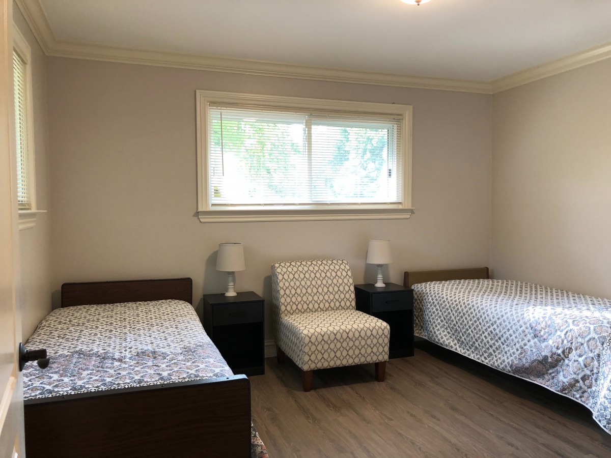 A minimalist bedroom with two beds, a window, and a chair between two nightstands.