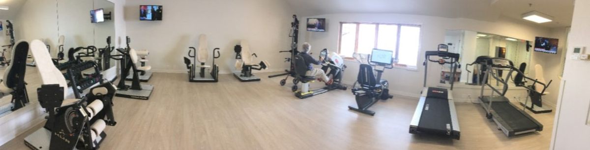 A person exercising on a rowing machine in a gym with various workout equipment.