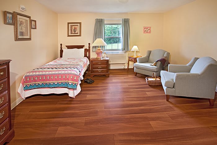 A cozy bedroom with a single bed, wooden floors, and a comfortable armchair.