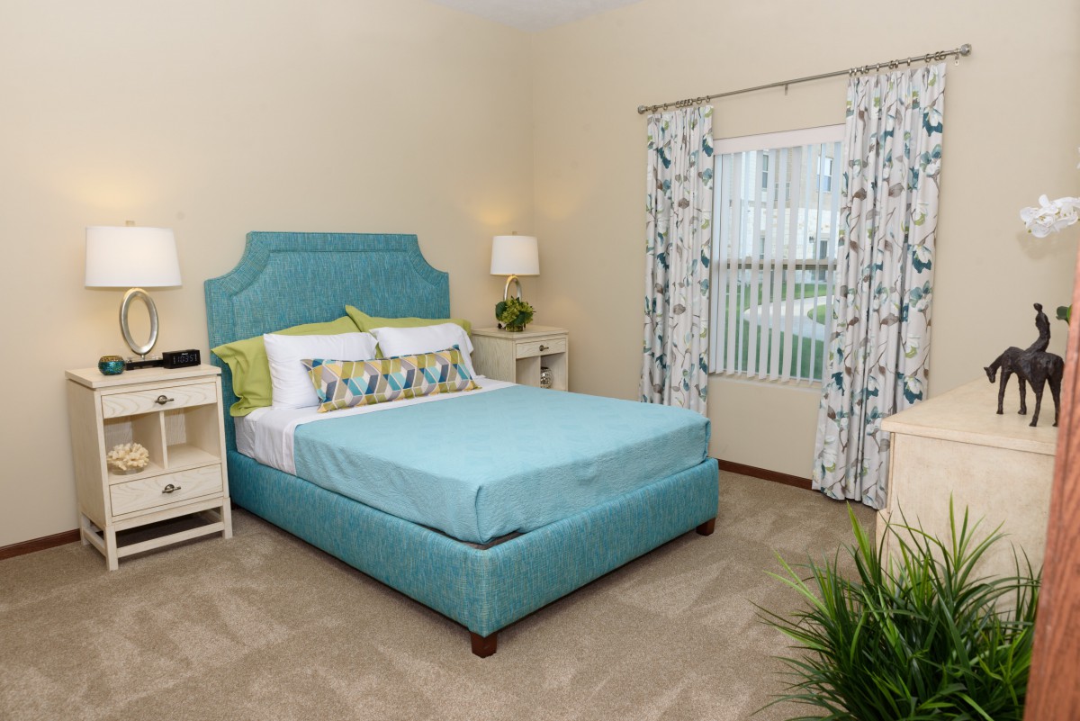 A cozy and well-decorated bedroom featuring a teal bed and matching headboard, complemented by patterned curtains and a bedside lamp.