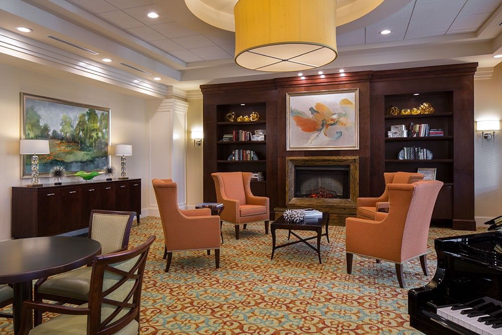 A cozy living room with a central fireplace, surrounded by armchairs and bookshelves, featuring elegant decor.