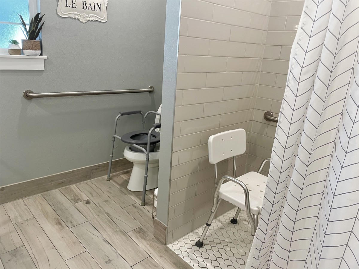 An accessible bathroom featuring a toilet and a shower with a shower chair and safety grab bars.