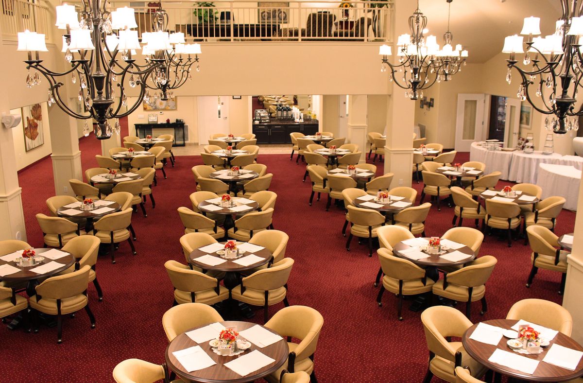 A spacious and elegantly designed restaurant dining area with chandeliers and neatly arranged tables and chairs on a red carpet.