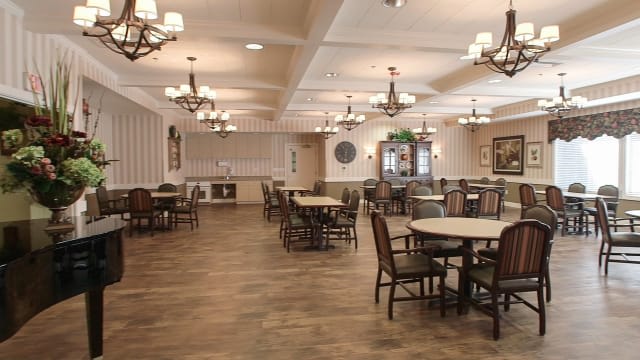 An empty dining area with multiple tables and chairs, featuring chandeliers and a wooden floor.