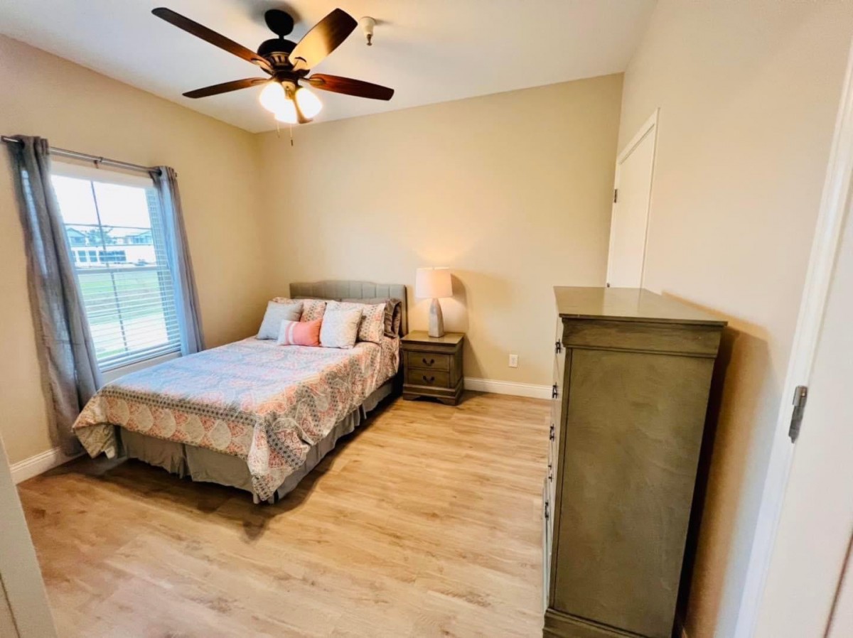 A modern bedroom with a comfortable bed, dresser, and ceiling fan.