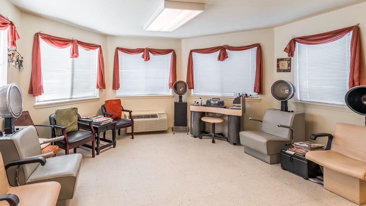 A retro-style salon interior with chairs and hair dryers, accented by red curtains on the windows.