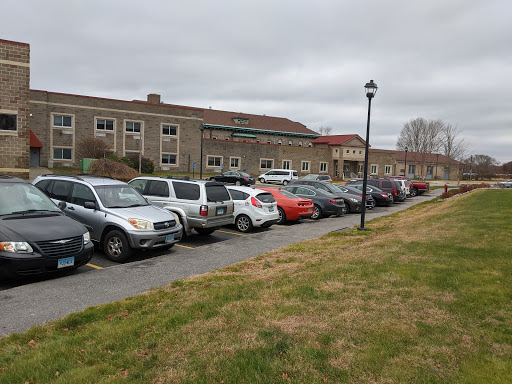 A view of a parking lot with various cars parked alongside a building, set against a cloudy sky.