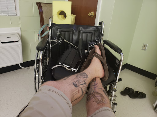 A casual moment with a focus on the legs adorned with tattoos, set against a backdrop including a wheelchair.