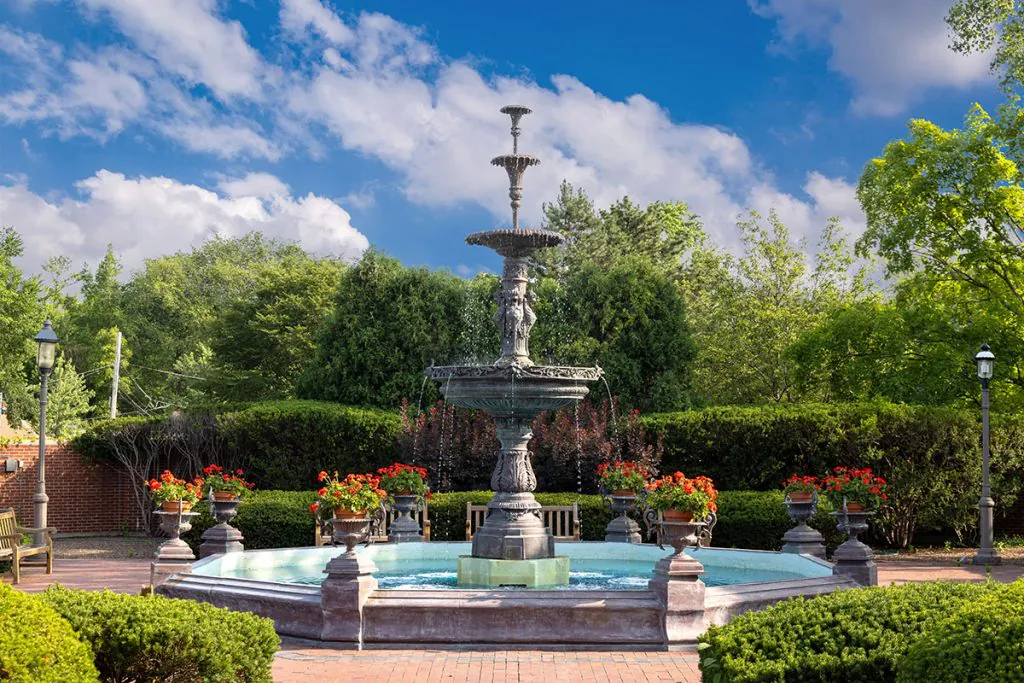 A decorative garden fountain surrounded by lush greenery and vibrant flowers under a clear blue sky.