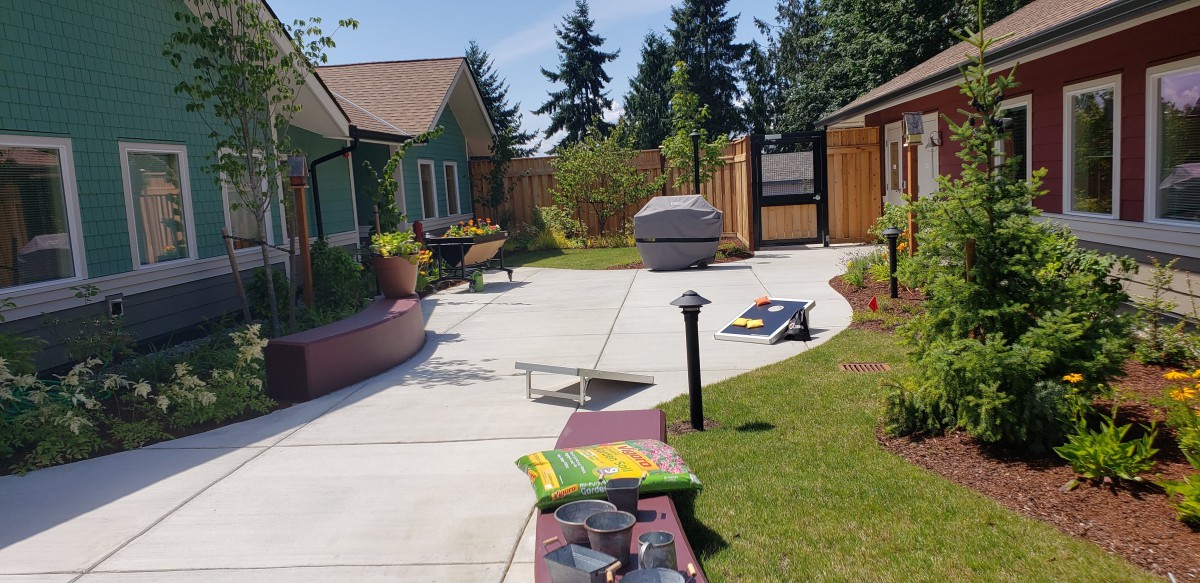 A sunny backyard with a cornhole setup and garden area.