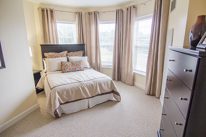A cozy bedroom with a neatly made bed and large windows adorned with curtains.