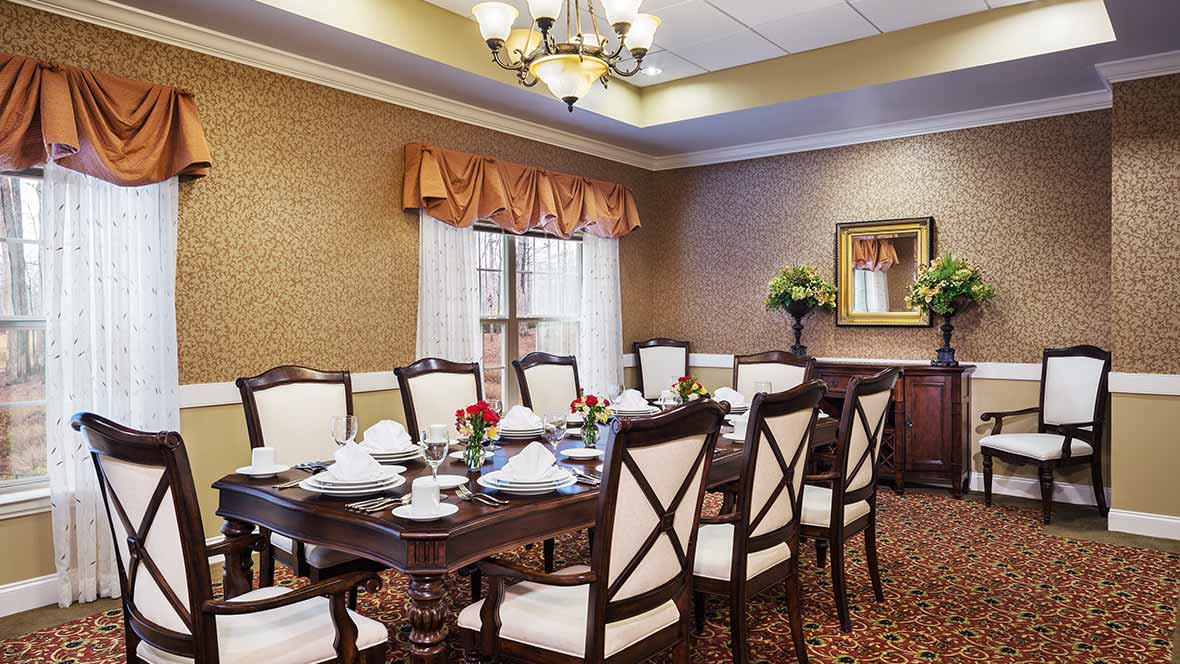 An elegant dining room with a formal table setting and wooden chairs, lit by a chandelier.