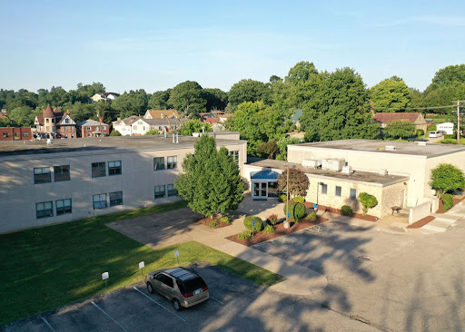 Aerial view of a modern building surrounded by greenery and a parking lot.