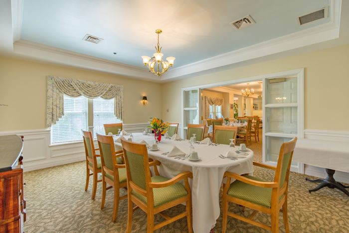 An elegantly decorated dining room with a set table and comfortable chairs, featuring soft lighting and large windows.