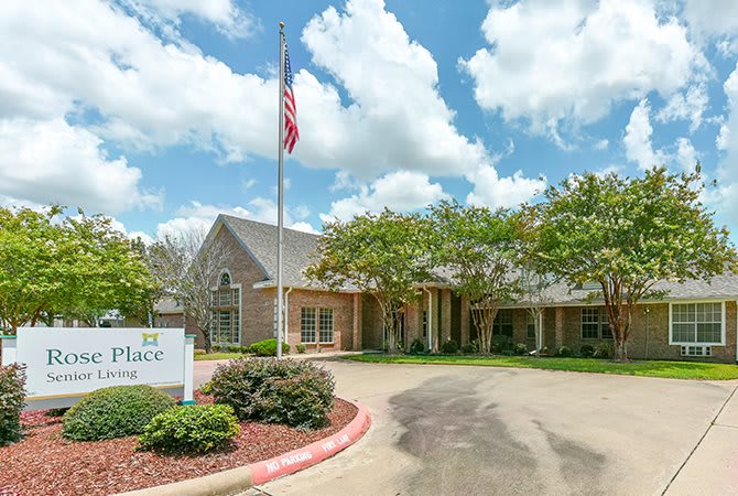 An exterior view of a building with an American flag, surrounded by trees and landscaped gardens, under a partly cloudy sky.