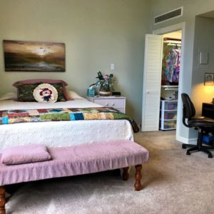 A cozy bedroom featuring a bed with a colorful quilt, an open closet, and a small desk with a chair.