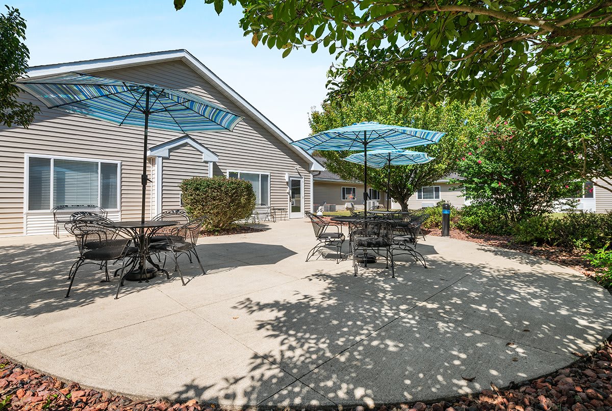 A serene outdoor patio area with tables, chairs, and blue umbrellas under the shade of trees.