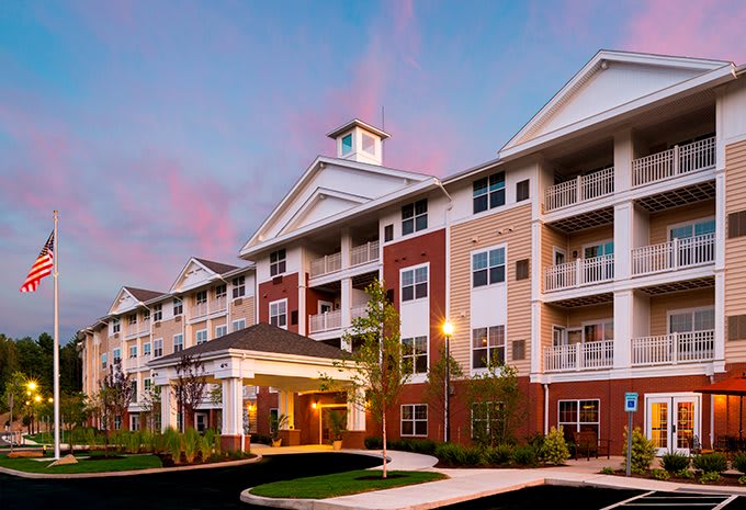 A modern apartment building with multiple floors and balconies, set against a sunset sky.