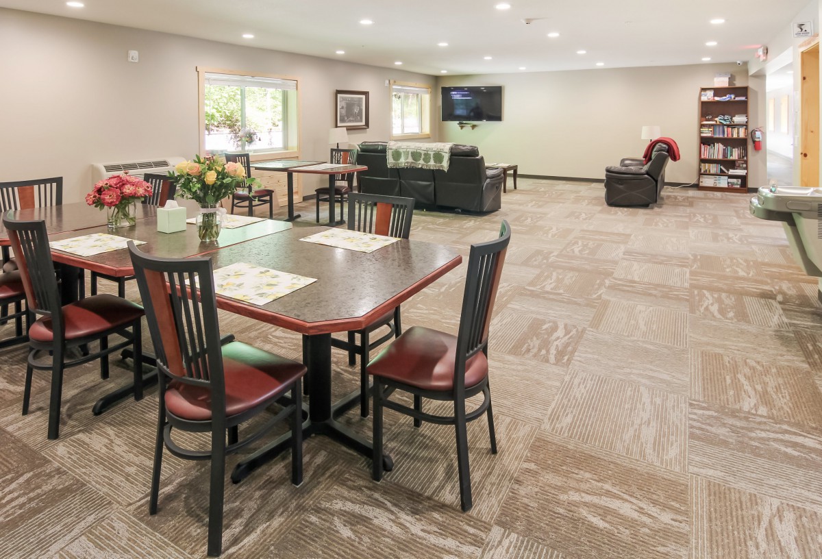 A spacious community room with dining tables, chairs, and a television.
