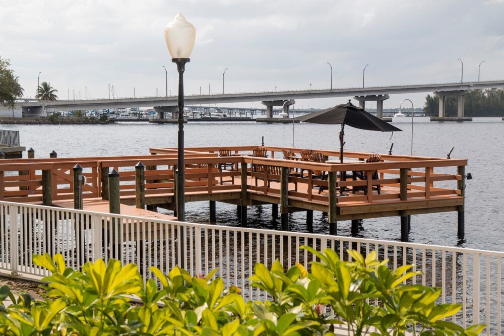 A scenic waterfront pier with outdoor seating and a view of a bridge in the background.