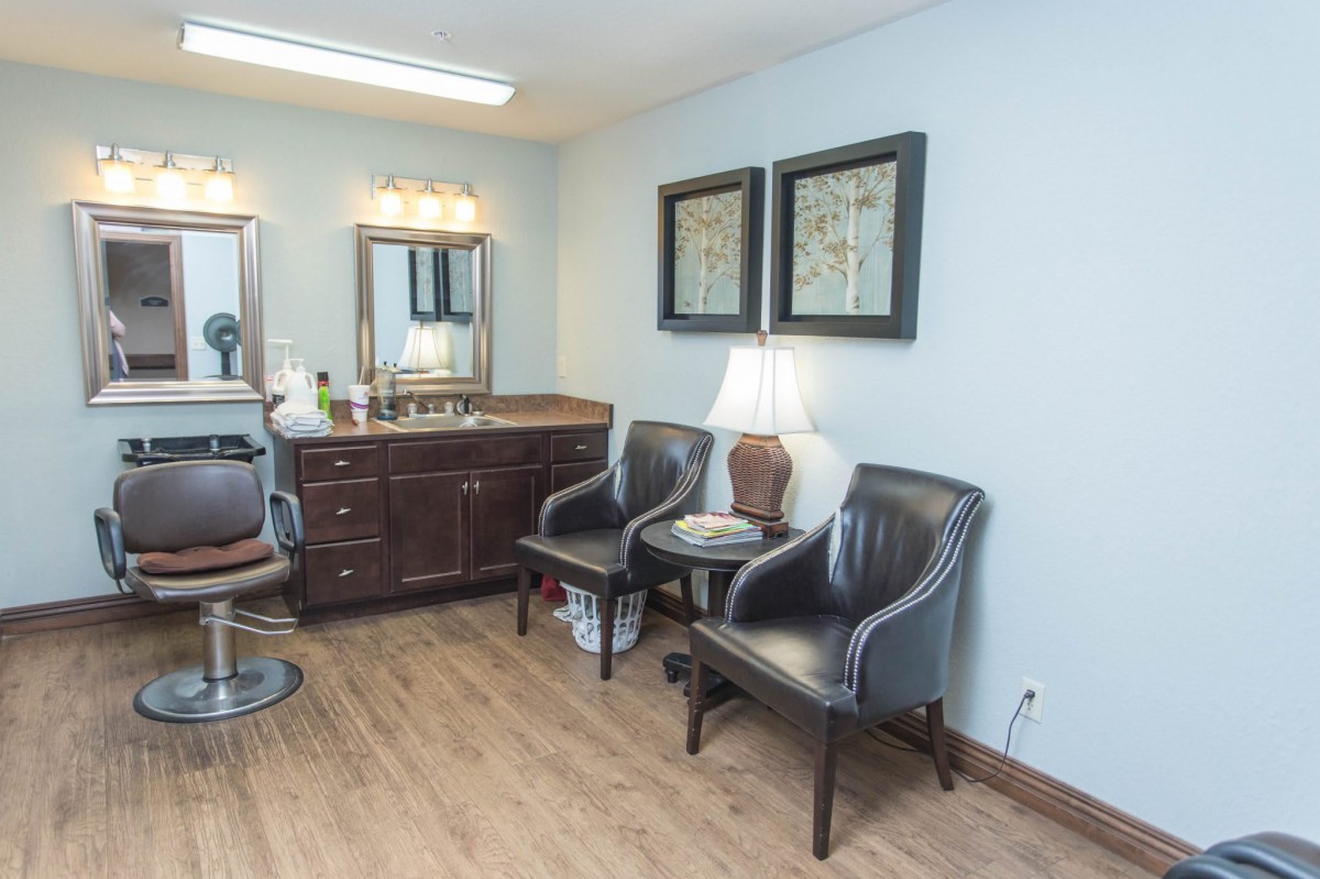 A cozy waiting room with chairs and a mirror, decorated with framed art and a lamp.