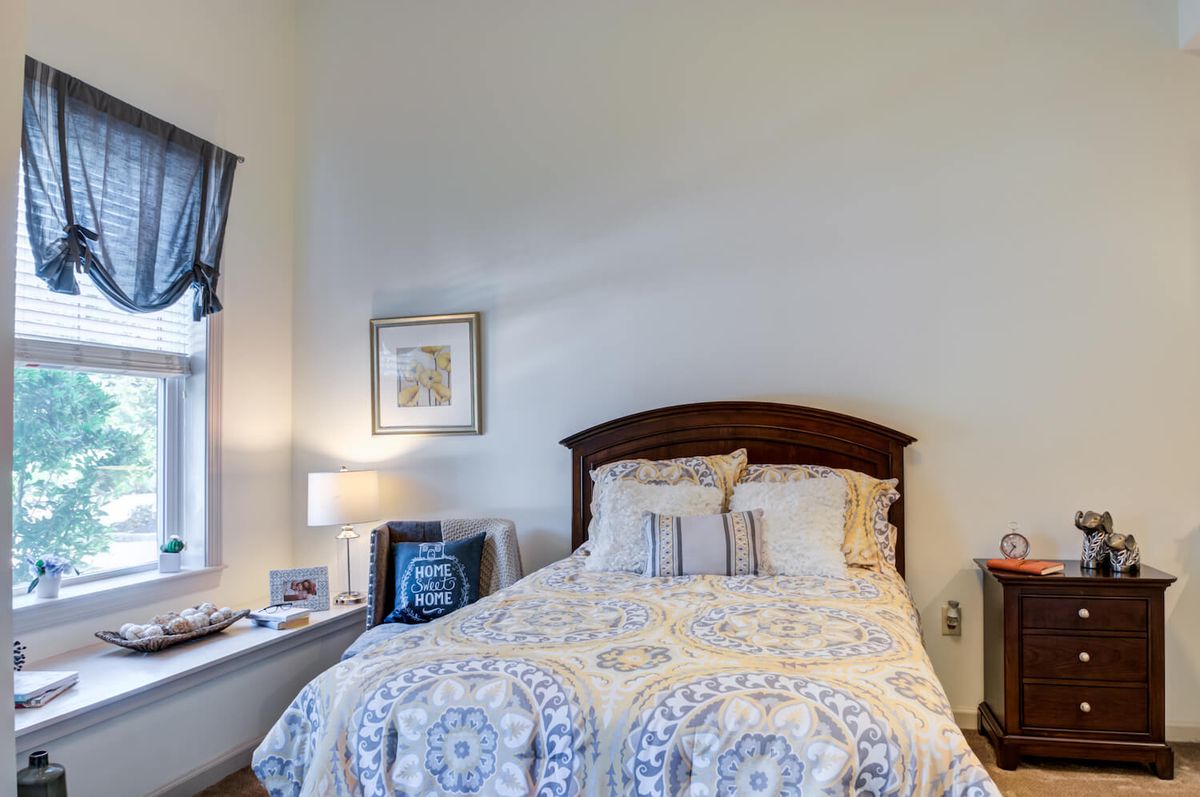 A cozy bedroom with a neatly made bed, bedside lamp, and wall art.
