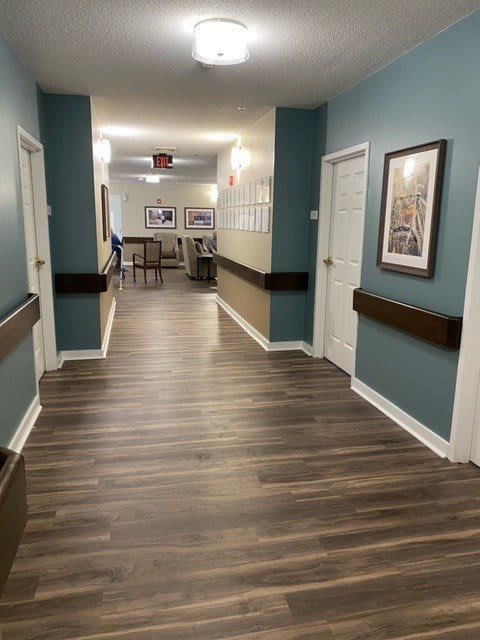 A modern hallway with wooden flooring and several doors, featuring artistic pictures on the walls and handrails for support.