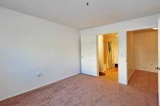 An empty room with carpeted flooring and white walls, featuring a doorway leading to another area.