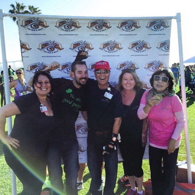 A group of friends posing together at an outdoor event in front of a banner.