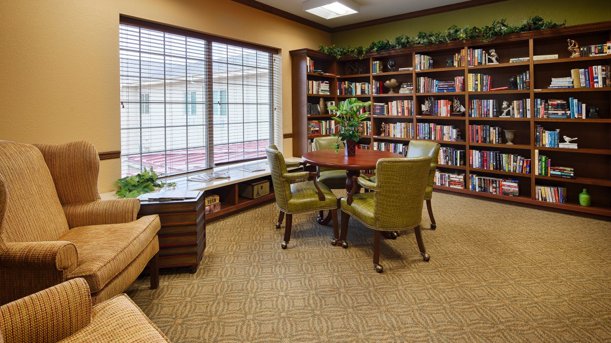 A cozy reading area in a library with bookshelves, chairs, and large windows.