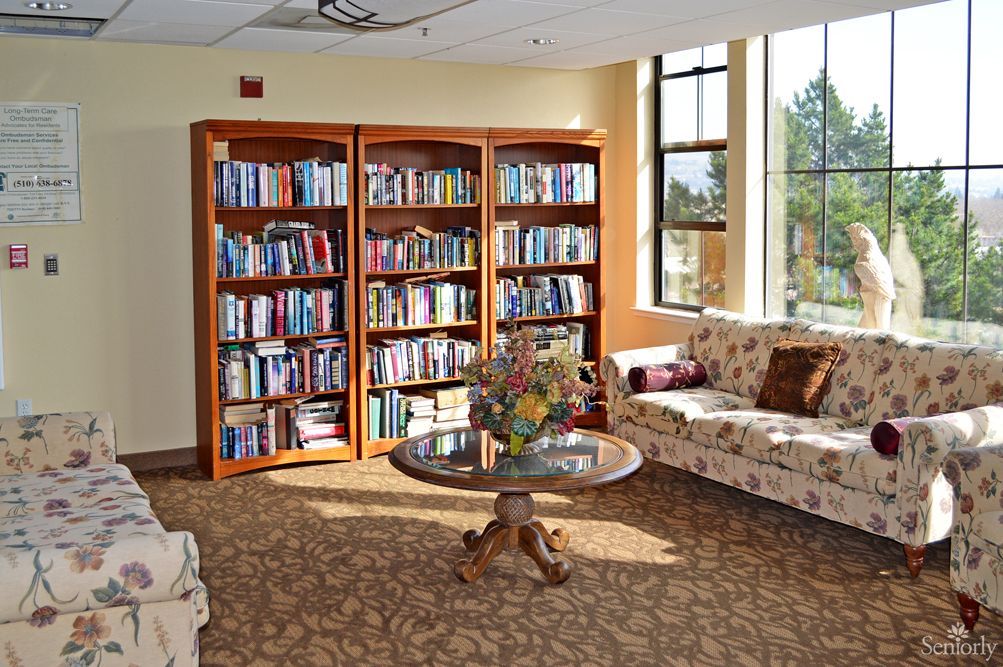 A cozy reading area with bookshelves filled with books, comfortable sofas, and a round table in a well-lit room.