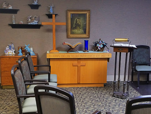 A serene chapel interior featuring an altar with a cross and seating for visitors.