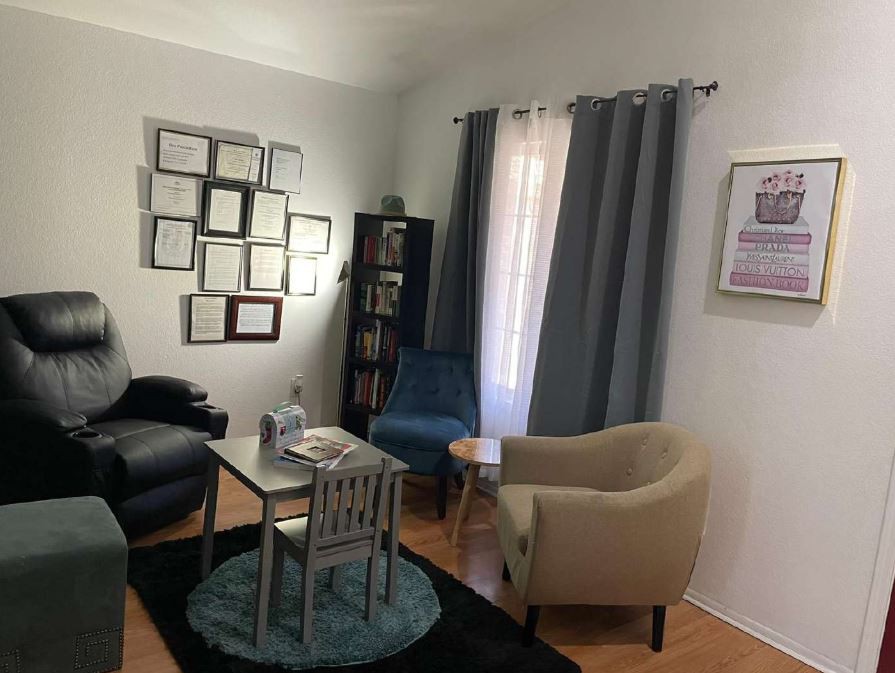 A cozy living room with a sofa, armchair, and coffee table, adorned with wall art and curtains.