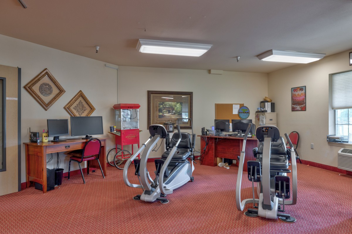 A multi-purpose room featuring exercise machines and a small office area.