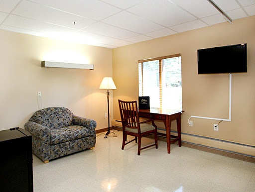 A cozy room with a sofa, wooden table and chair, lamp, and a TV, featuring a window that provides natural light.