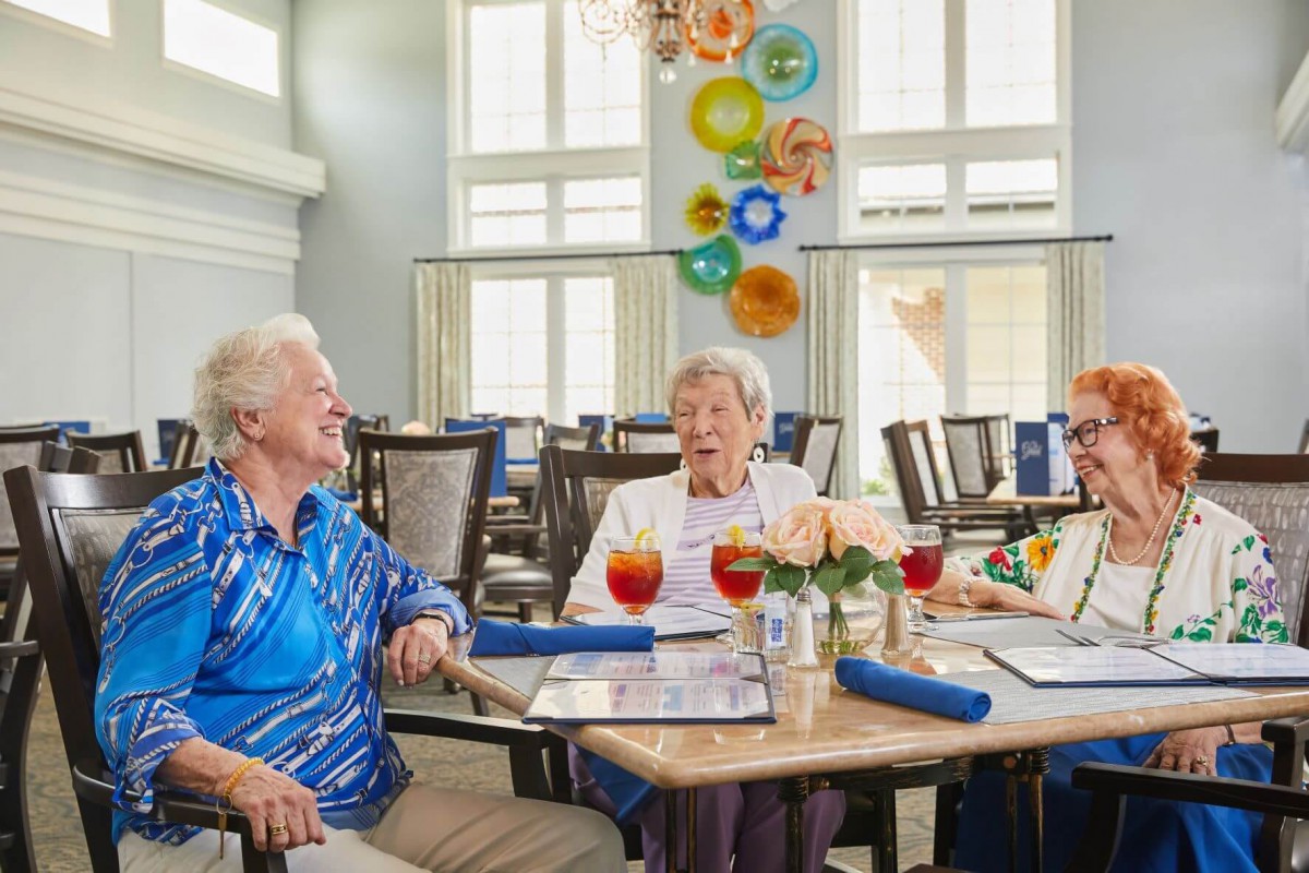 A group of seniors enjoying conversation and drinks in a dining setting.