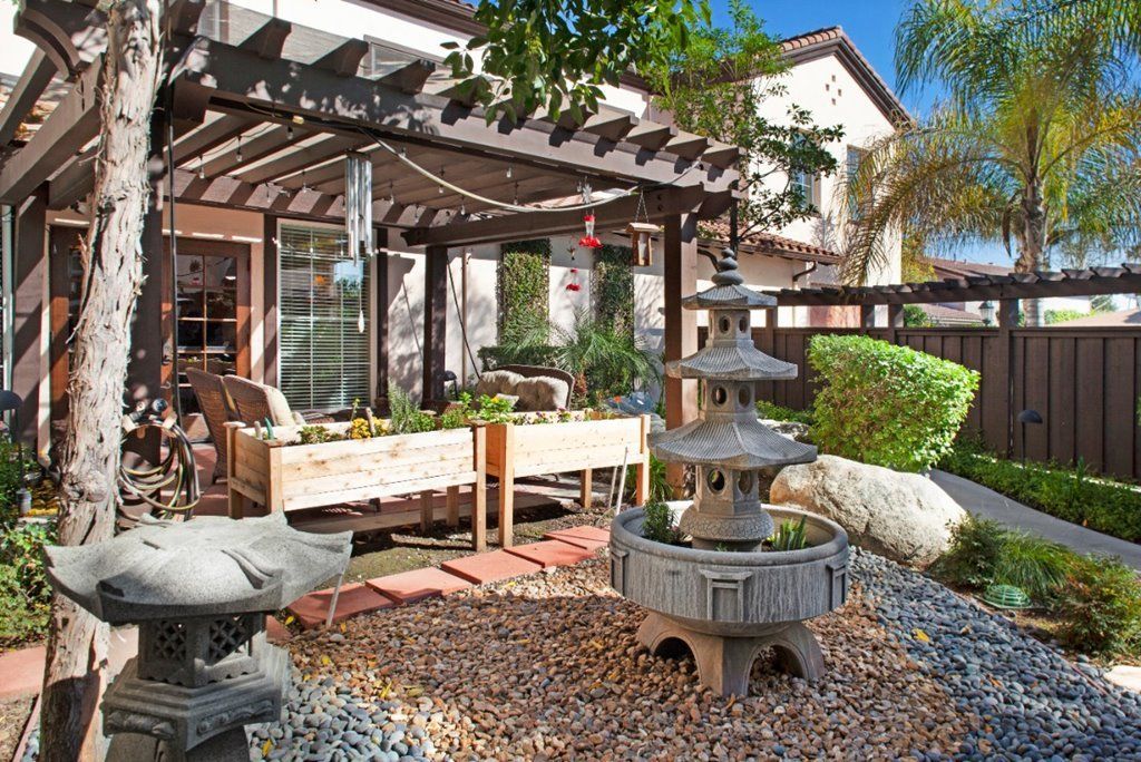A serene outdoor patio featuring a pergola, zen-style fountain, and lush landscaping.