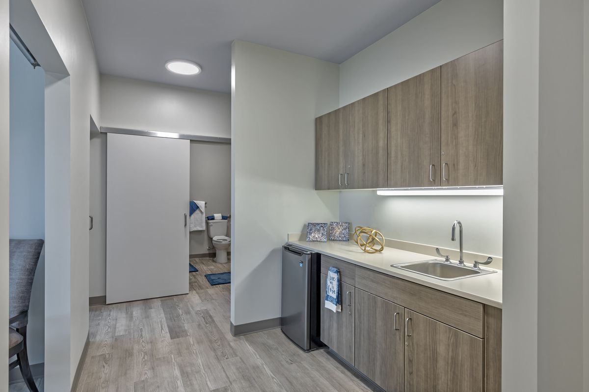 A modern, compact kitchen area with wooden cabinets and a small refrigerator.