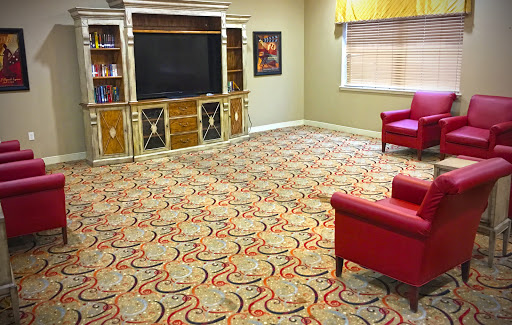 A cozy living room featuring a red chair, a large television, and an intricately patterned carpet.