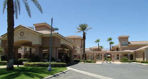 A sunny entrance to a hotel, surrounded by palm trees and clear blue skies.