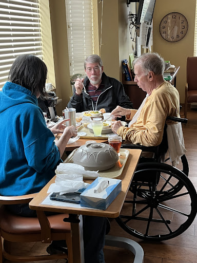 A group of three individuals enjoying a meal together, including one person in a wheelchair.