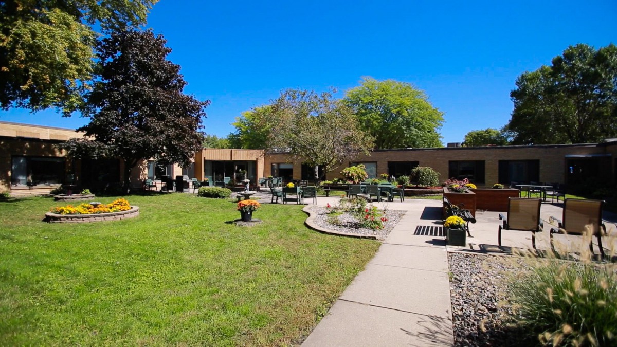 A peaceful garden with a patio and surrounding trees under a clear blue sky.
