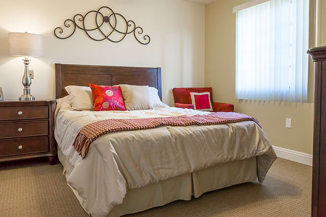 A cozy bedroom with a neatly made bed, decorative pillows, and a comfortable chair by the window.