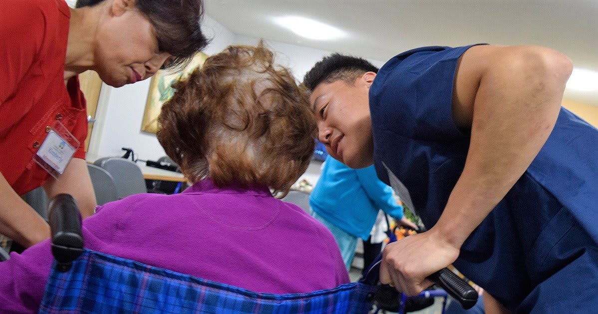 A caregiver interacts warmly with an elderly person in a nursing home setting.
