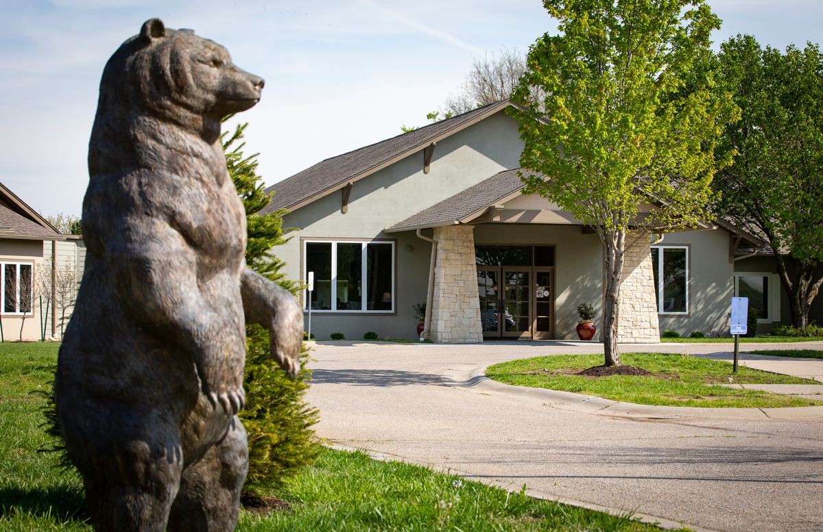 A bear statue stands guard outside a modern building surrounded by greenery.