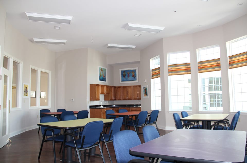 A spacious dining area with tables and chairs, featuring large windows and a kitchenette.