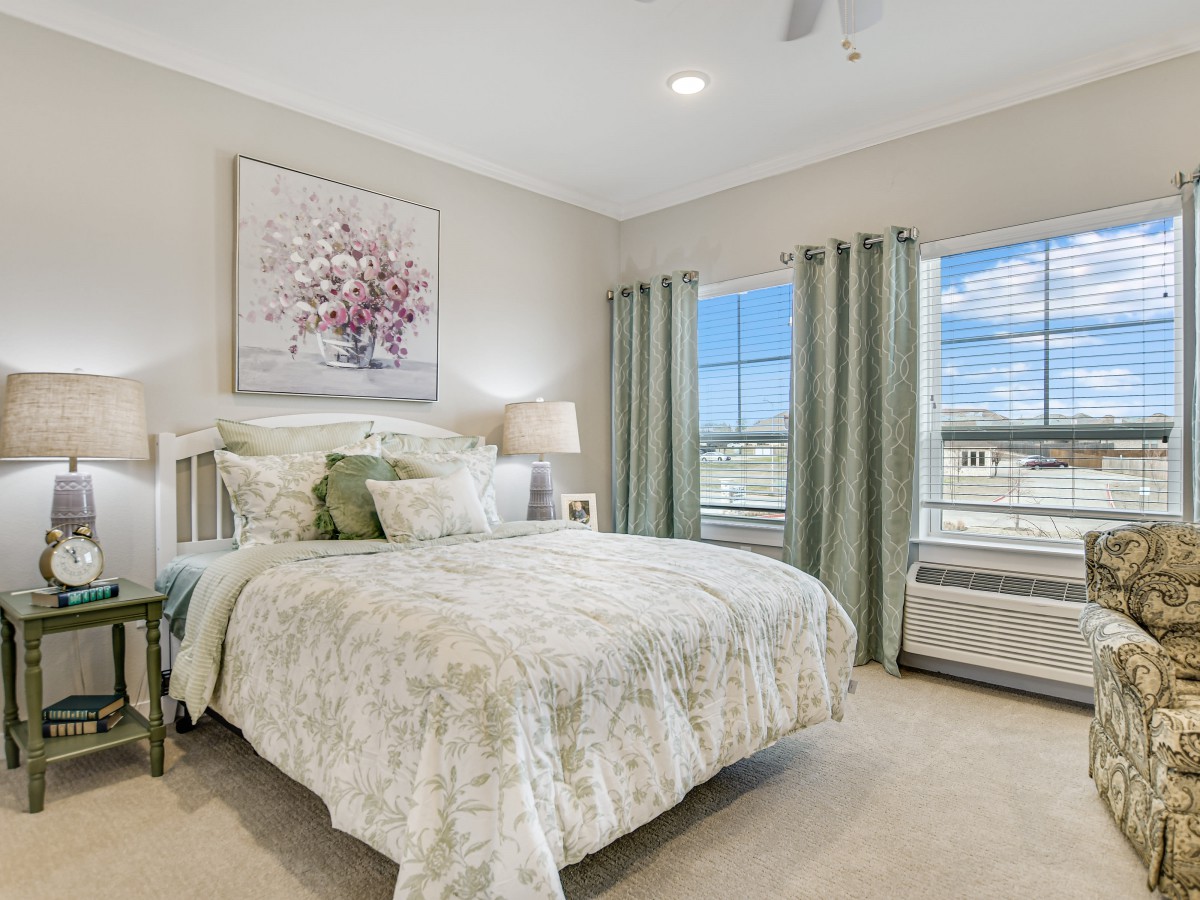 A beautifully decorated bedroom featuring a comfortable bed with floral bedding, soft lighting, and elegant curtains framing the windows.