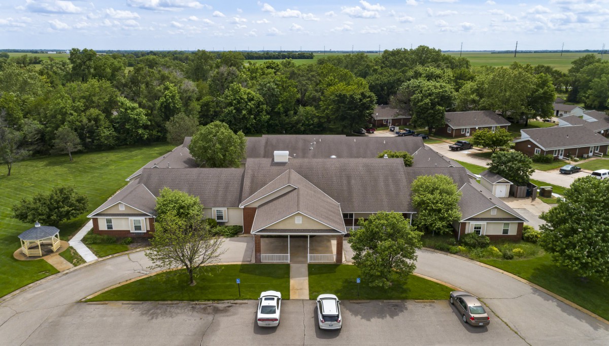 Aerial view of a residential building surrounded by trees with a parking lot at the front.