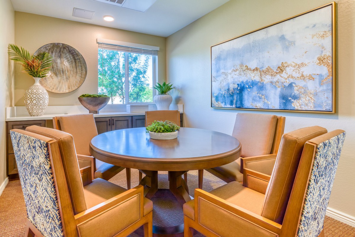 A cozy meeting room with a round table surrounded by chairs, featuring artwork and plants.