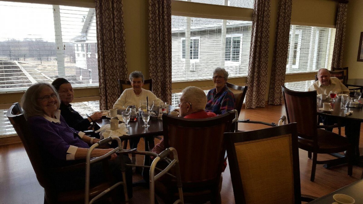A group of seniors sitting together in a dining room, engaged in conversation.